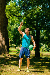 Active and muscular man keeping fit by exercising using a medicine ball. Working out outside in the summer.