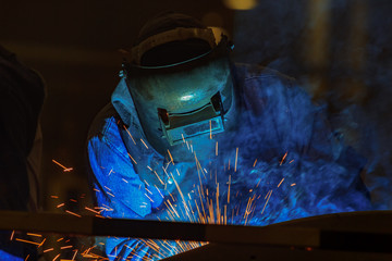 Industrial worker is welding automotive part in factory