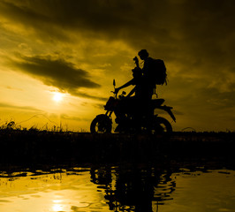 Obraz na płótnie Canvas Silhouette Two brothers with a backpack riding a motorbike while the sun sets.