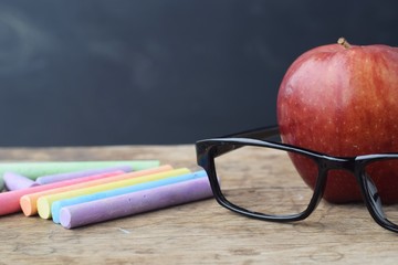 red apple with black glasses and chalk sticks on rustic wood table  background, smart education or teacher's day concept