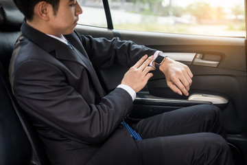 Handsome businessman looking on wrist watch in car.