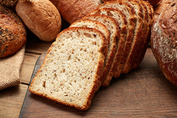 heap of whole and sliced fresh baked bread on wooden background