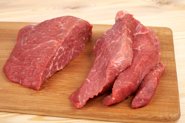 Raw beef piece and slices on wooden cutting board