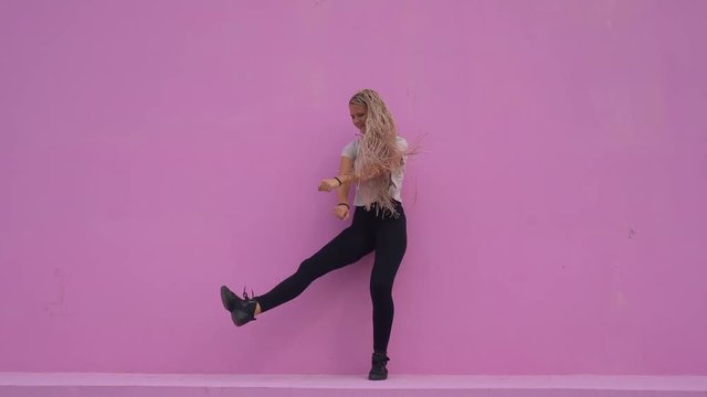 Casual girl with braided hair having fun and silly dancing over pink background