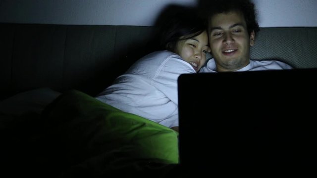 A couple talking in bed at night while watching a bright laptop screen