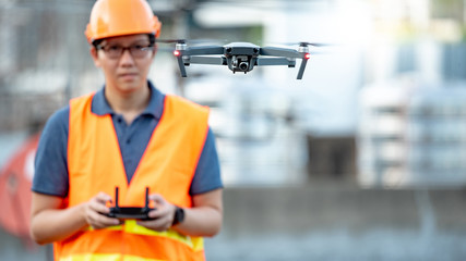 Young Asian engineer man flying drone over construction site. Using unmanned aerial vehicle (UAV) for land and building site survey in civil engineering project.