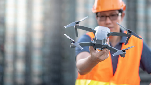 Young Asian engineer man holding drone at construction site. Using unmanned aerial vehicle (UAV) for land and building site survey in civil engineering project.