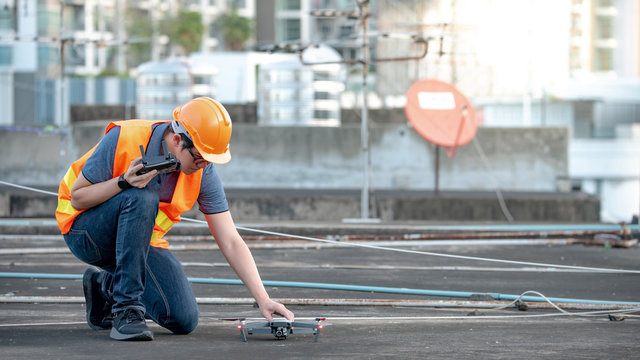 Young Asian engineer man setting up drone at construction site. Using unmanned aerial vehicle (UAV) for land and building site survey in civil engineering project.