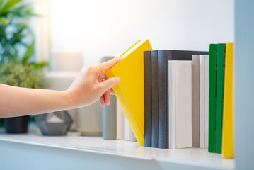 Male hand choosing and picking white book on white bookshelf in public library, education research and self learning in university life concepts © zephyr_p
