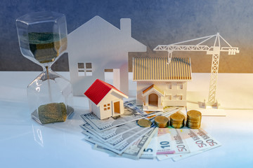 Real estate or property development. Construction business investment concept. Home mortgage loan rate. Coin stack on international banknotes with hourglasses, house and crane models on the table.