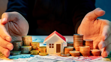 Real estate or property investment growing business. Home mortgage loan rate. Saving money for retirement concept. male hand holding house model and coin stack on international banknotes on table