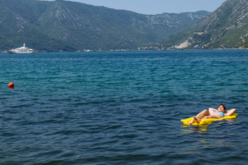 young adult woman on yellow mattress in blue sea water.