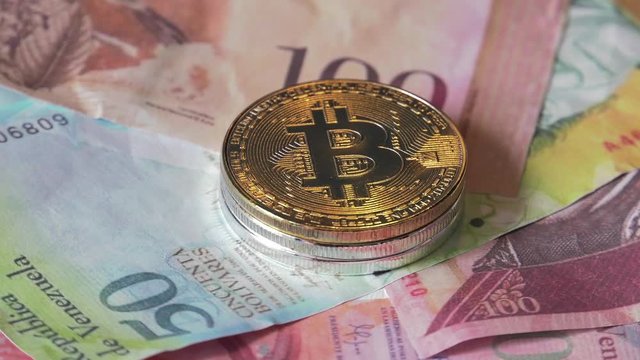 Physical metal Bitcoin currency over bolivar bills. Virtual internet money with Venezuelan banknotes. Digital coin cyberspace, cryptocurrency. BTC golden coin as symbol of electronic virtual money. 4K