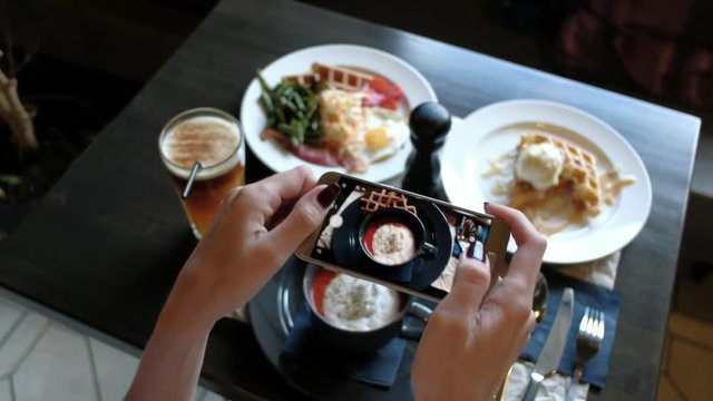 Female hands photographing appetizing food by smartphone in the restaurant.