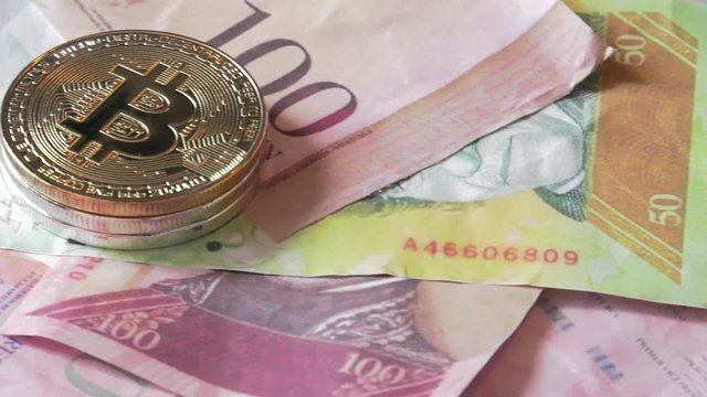 Physical metal Bitcoin currency over bolivar bills. Virtual internet money with Venezuelan banknotes. Digital coin cyberspace, cryptocurrency. BTC golden coin as symbol of electronic virtual money. 4K