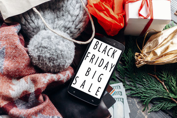 black friday big sale. special christmas offer discount text on mobile phone screen message on seasonal rustic background with money cards wallet and bag with stuff and presents. advertising concept.