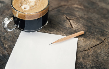 Pencil on blank white note with cup of coffee on wooden table