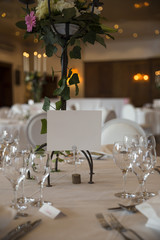 elegantly served with glasses, cutlery and decorated with flowers tables with white tablecloths and burning candles in candlesticks in the blurred background of the fashionable restaurant hall
