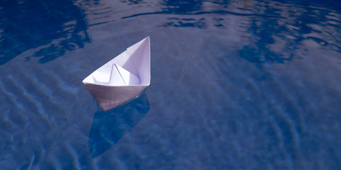 Paper boat - origami ship on blue water with ripples and copy space