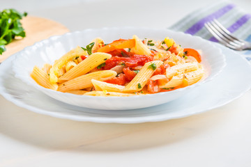 Italian food - pasta with peppers and tomatoes in a plate on a light background, penne