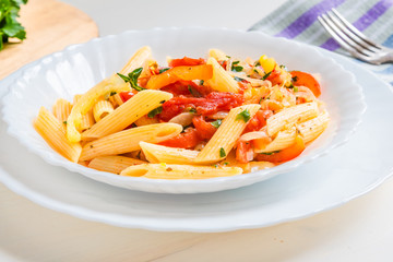 Italian food - pasta with peppers and tomatoes in a plate on a light background, penne