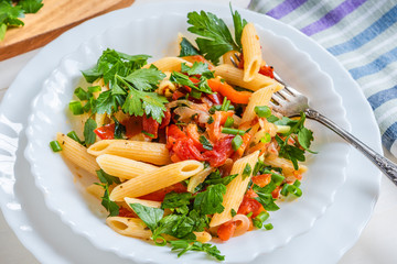 Italian food - pasta with peppers and tomatoes and parsley in a plate on a light background, penne