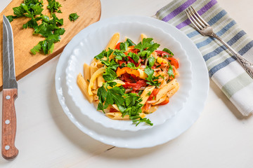 Italian food - pasta with peppers and tomatoes and parsley in a plate on a light background, penne