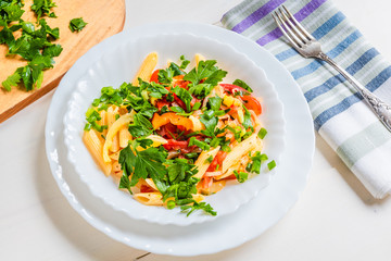 Italian food - pasta with peppers and tomatoes and parsley in a plate on a light background, penne