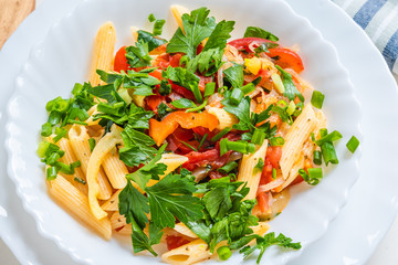 Traditional Italian pasta with peppers and tomatoes and parsley in a bowl close-up, penne
