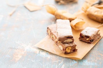 A variety of different nutty nougat in dark chocolate with roasted hazelnuts cut open to show the nougat mix on a wooden board . Copy space.