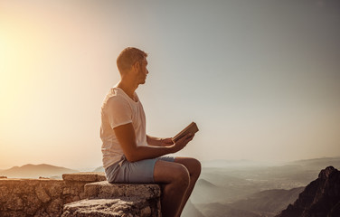 Naklejka na ściany i meble sitting book reading man over the mountains on sunset