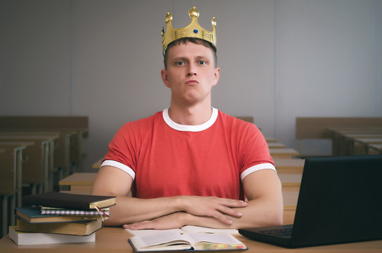 Arrogant student boy with golden crown above his head with an insolent look sits at a desk. Bad behavior in school concept.