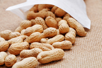 Peanuts poured from a white bag on a sacking background