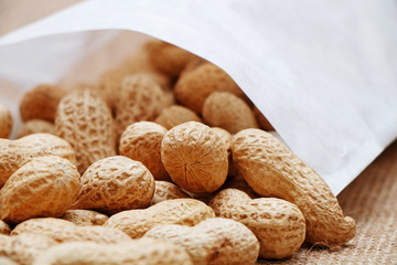 Peanuts poured from a white bag on a sacking background