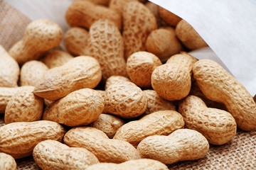 Peanuts poured from a white bag on a sacking background