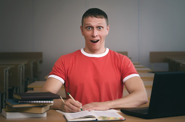 Amazed student boy sitting by the school desk.