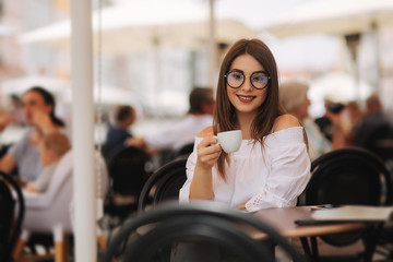 Close up fashion image of woman holding white cup of her morning cappuccino, wearing white stylish clothes and vintage sunglasses. Enjoy her time alone. Instagram colors