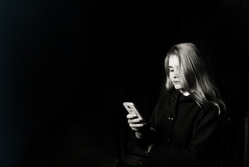 young scared and worried teenager girl holding mobile phone as internet stalked victim abused and cyberbullying or cyber bullying stress concept in black background