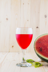 Watermelon juice in a wine glass with half water melon on wood floor