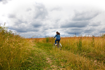 Happy Young Woman riding bicycle on a yellow field. Healthy Lifestyle.