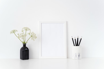 Modern white portrait a4 frame mock up with a herbal gerard in black vase and black pencils near white wall.