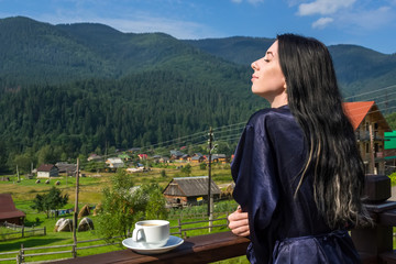 young, beautiful, sleepy woman drinks coffee on a background of mountains in the early morning