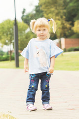 cheerful little blonde with two tails walking along the alley in the city park in summer sunny weather
