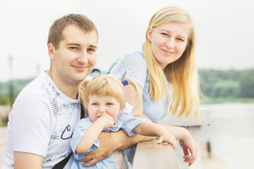 Young couple mom and dad playing with a small beautiful blonde girl in a sunny summer rain in a city park by the river