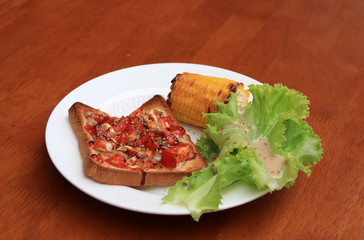 Home made pizza on sliced bread with grilled Corn and lettuce in the white round plate on the wooden table. Incline angle.