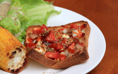 Home made pizza on sliced bread with grilled Corn and lettuce in the white round plate on the wooden table. Close up.