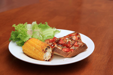 Home made pizza on sliced bread with grilled Corn and lettuce in the white round plate on the wooden table. Incline angle.