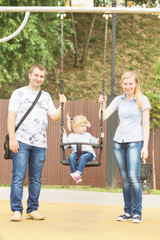 Young couple mom and dad playing with a small beautiful blonde girl in a sunny summer rain in a city park by the river