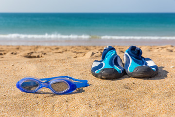 Fototapeta na wymiar Swimming goggles and water shoes on beach at sea