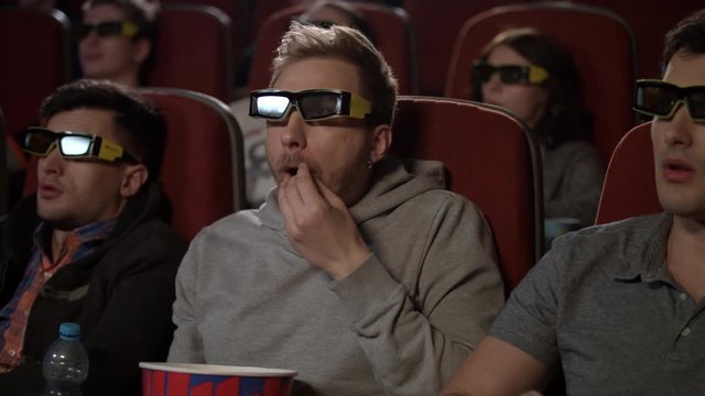Cinema friends watching 3d movie. People in 3d glasses at cinema. Man in 3d glasses eat pop corn. Man eating popcorn at multiplex movie. Male friends enjoy exciting film